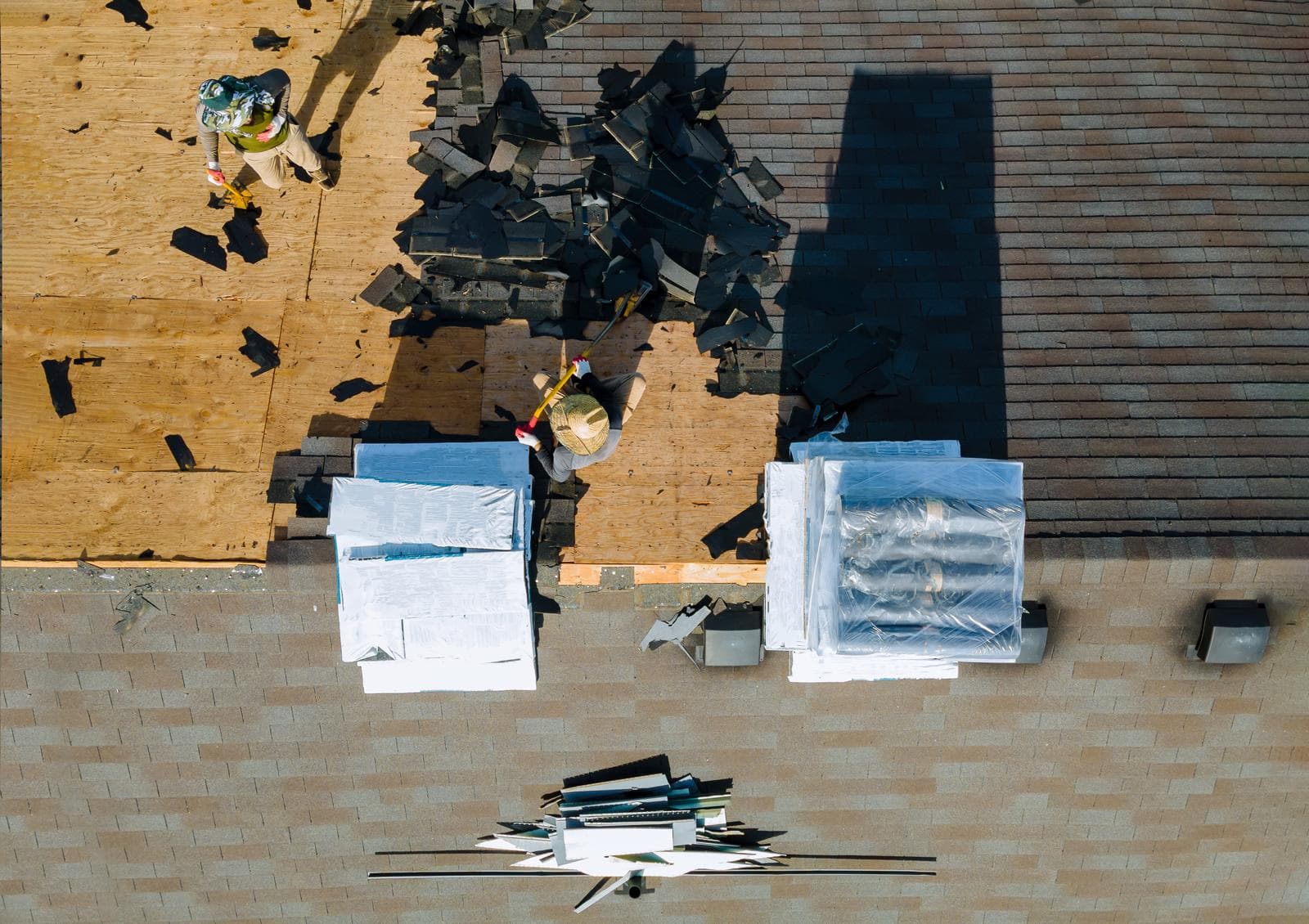 Aerial view of roof damage with scattered shingles and repair materials