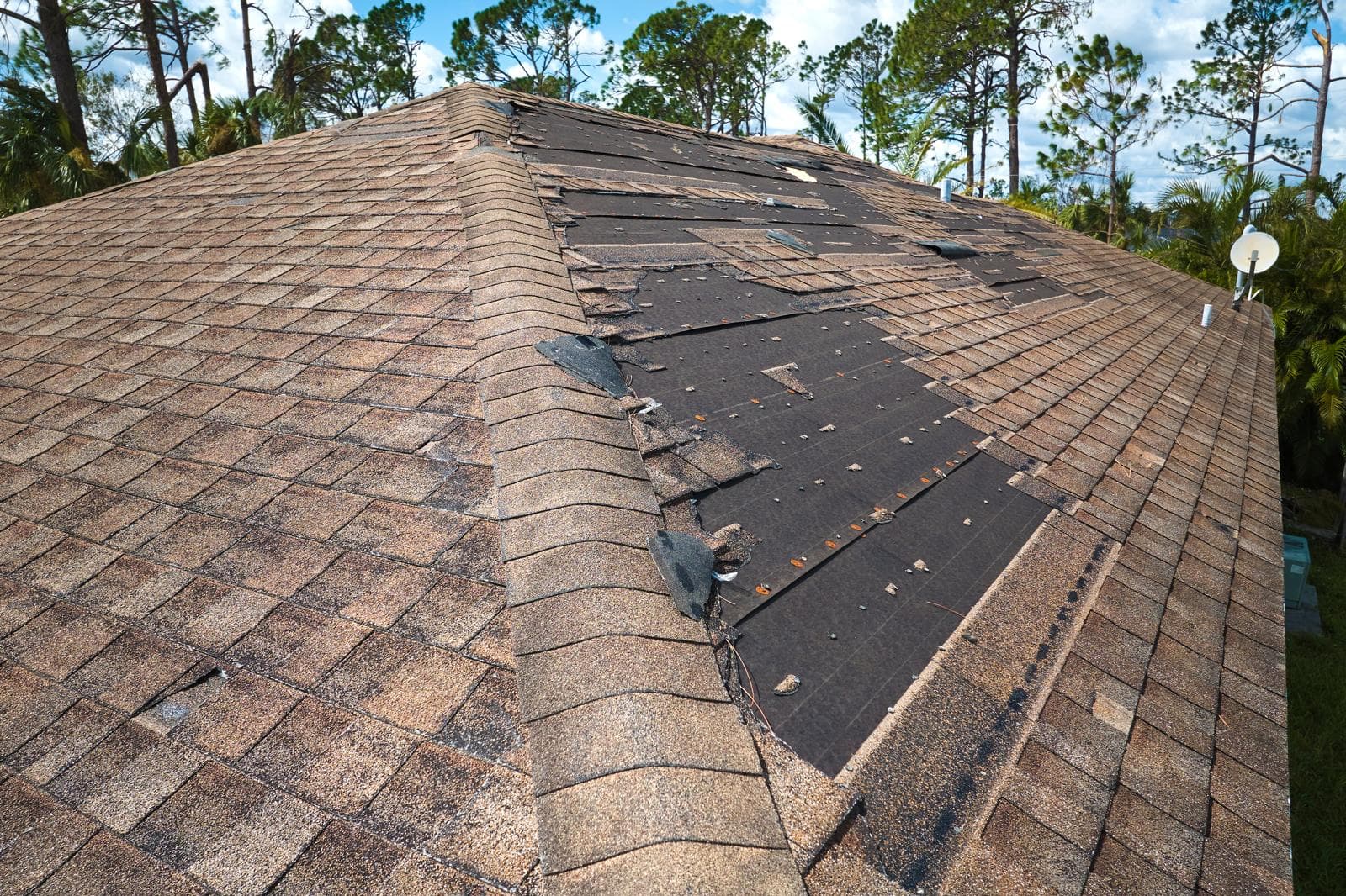 Hurricane damaged roof with missing shingles and exposed areas